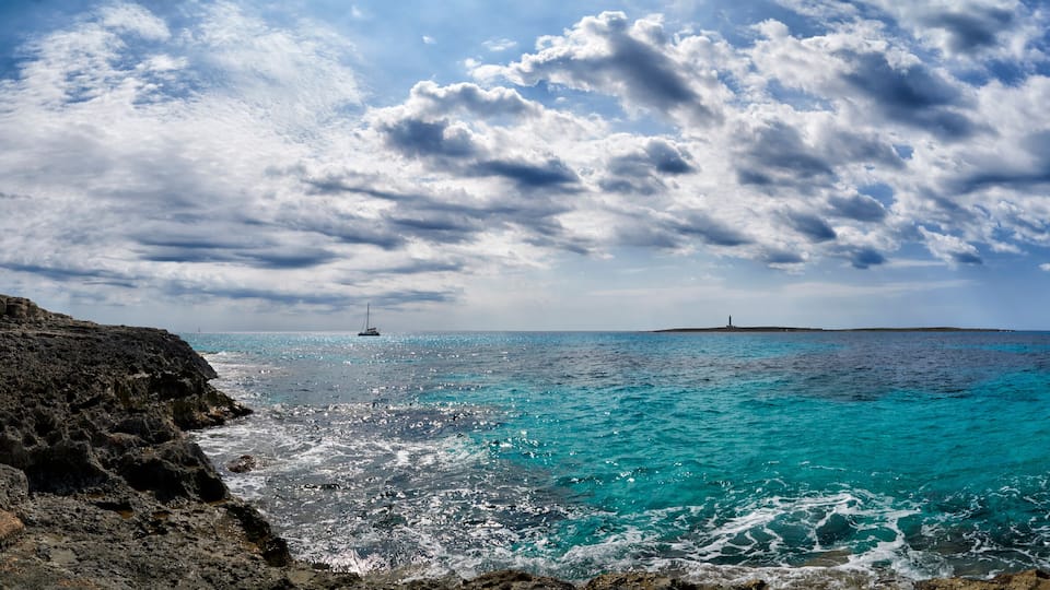A coastal landscape with turquoise waters, rocky cliffs, and a lighthouse in the distance.
