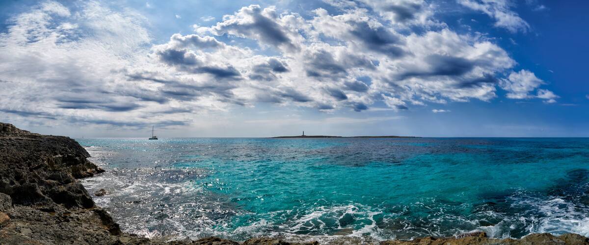A coastal landscape with turquoise waters, rocky cliffs, and a lighthouse in the distance.