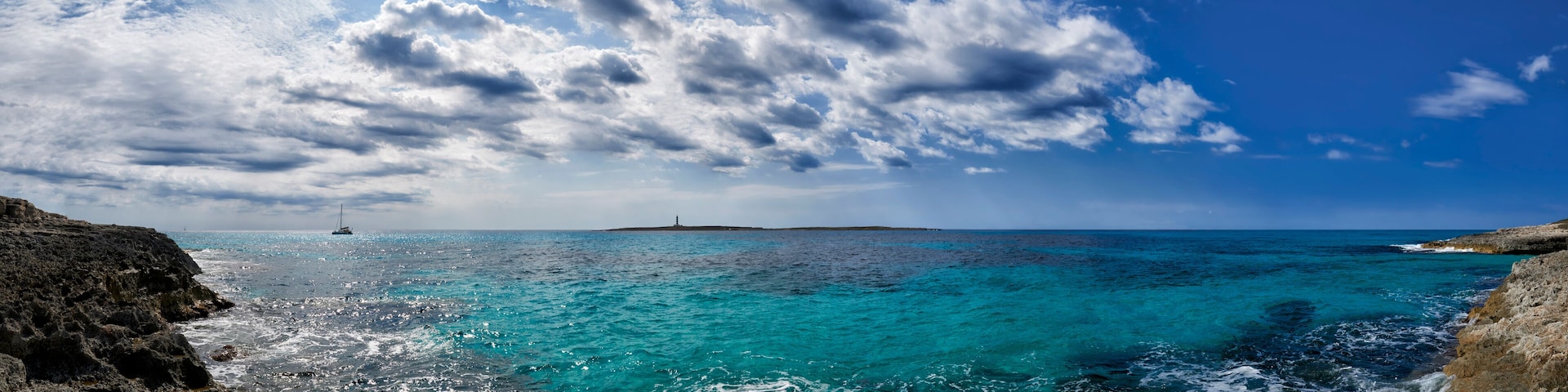 A coastal landscape with turquoise waters, rocky cliffs, and a lighthouse in the distance.
