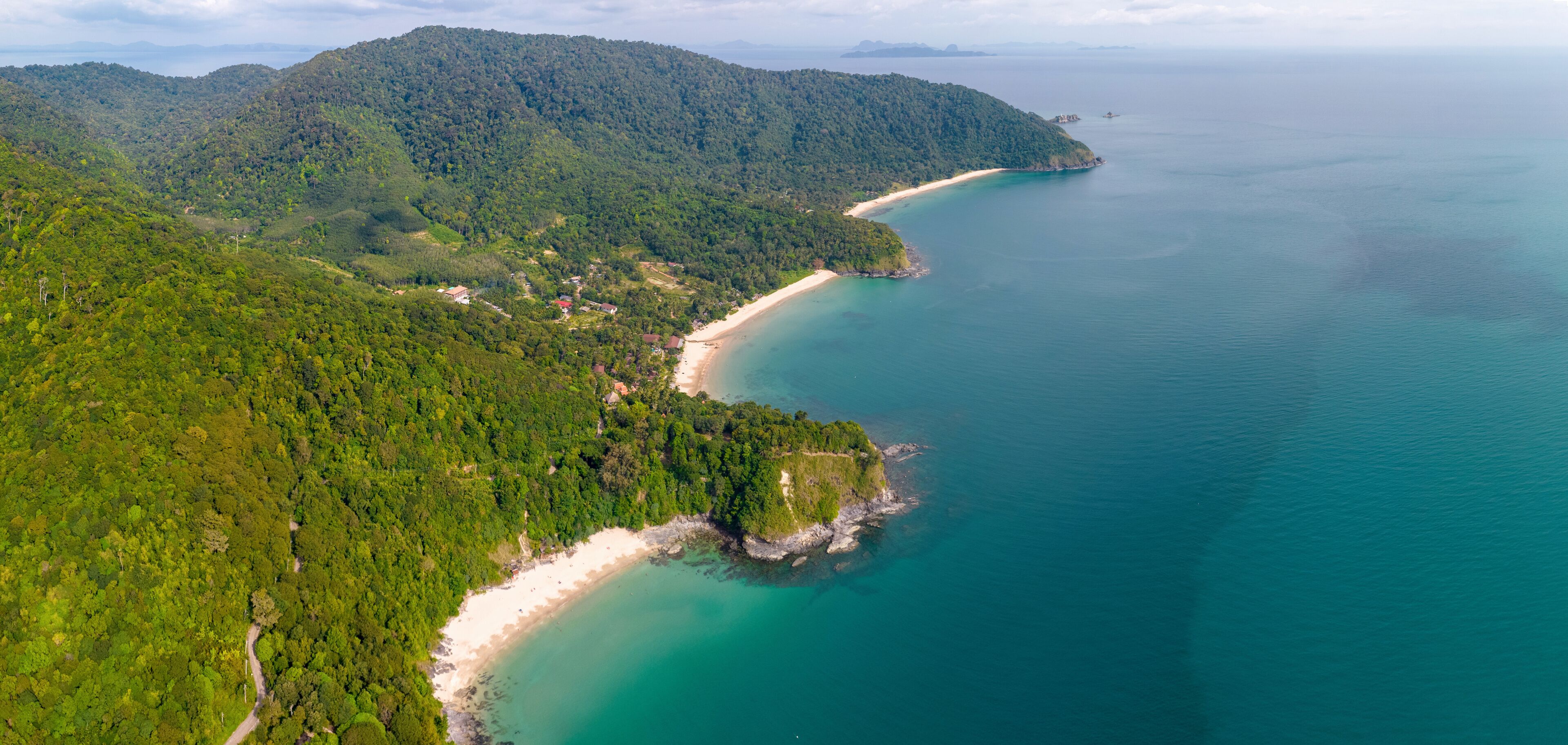 A coastal landscape with a beach, dense forest, and a clear view of the sea.