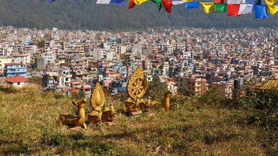 A cityscape with colorful prayer flags and golden statues in the foreground.