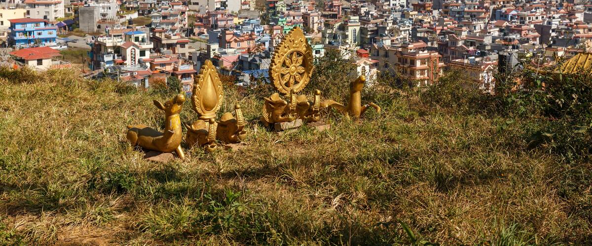 A cityscape with colorful prayer flags and golden statues in the foreground.