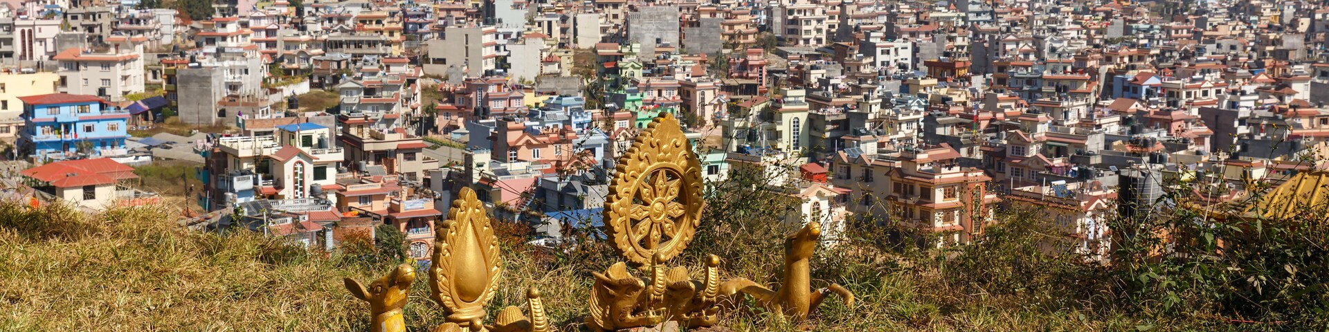 A cityscape with colorful prayer flags and golden statues in the foreground.