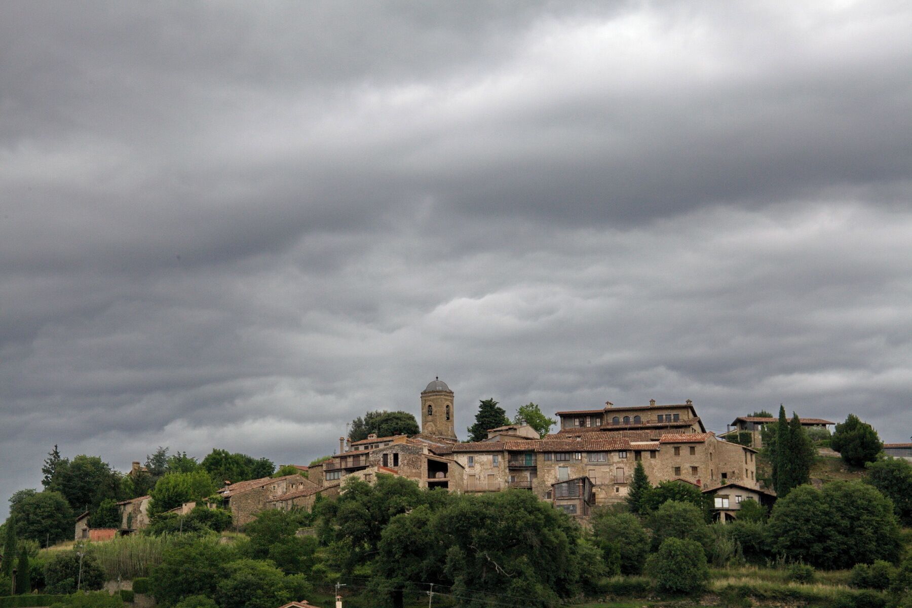 A historic village with stone buildings and a prominent church tower under a cloudy sky.
