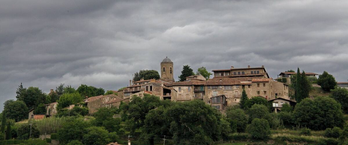 A historic village with stone buildings and a prominent church tower under a cloudy sky.
