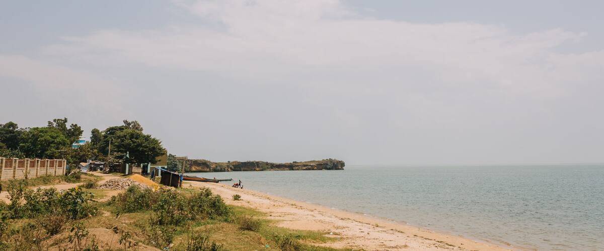 A beach with a sandy shore, a few boats, and some buildings in the background.