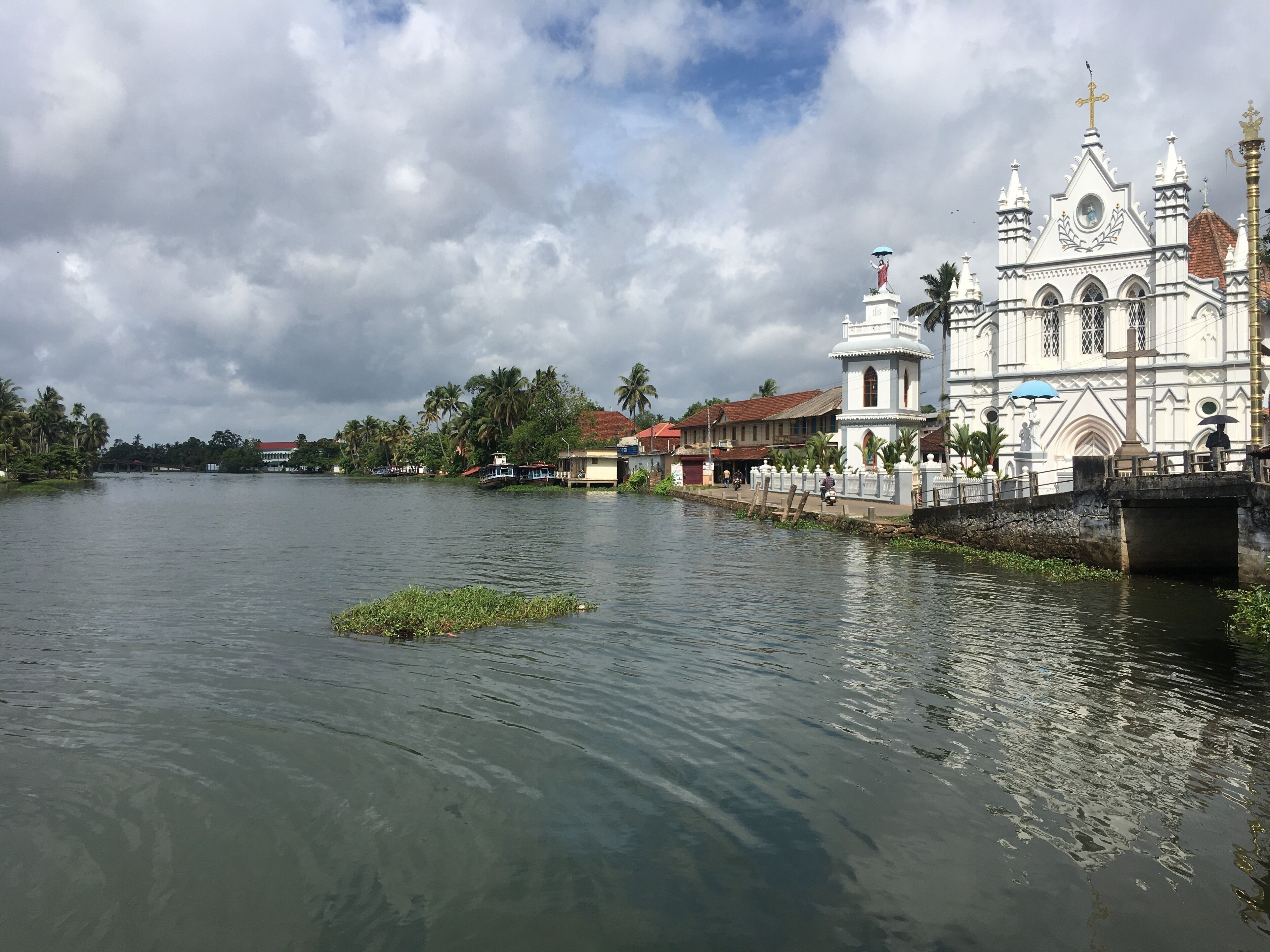 A river with a small island, a white church with a cross, and palm trees in the background.