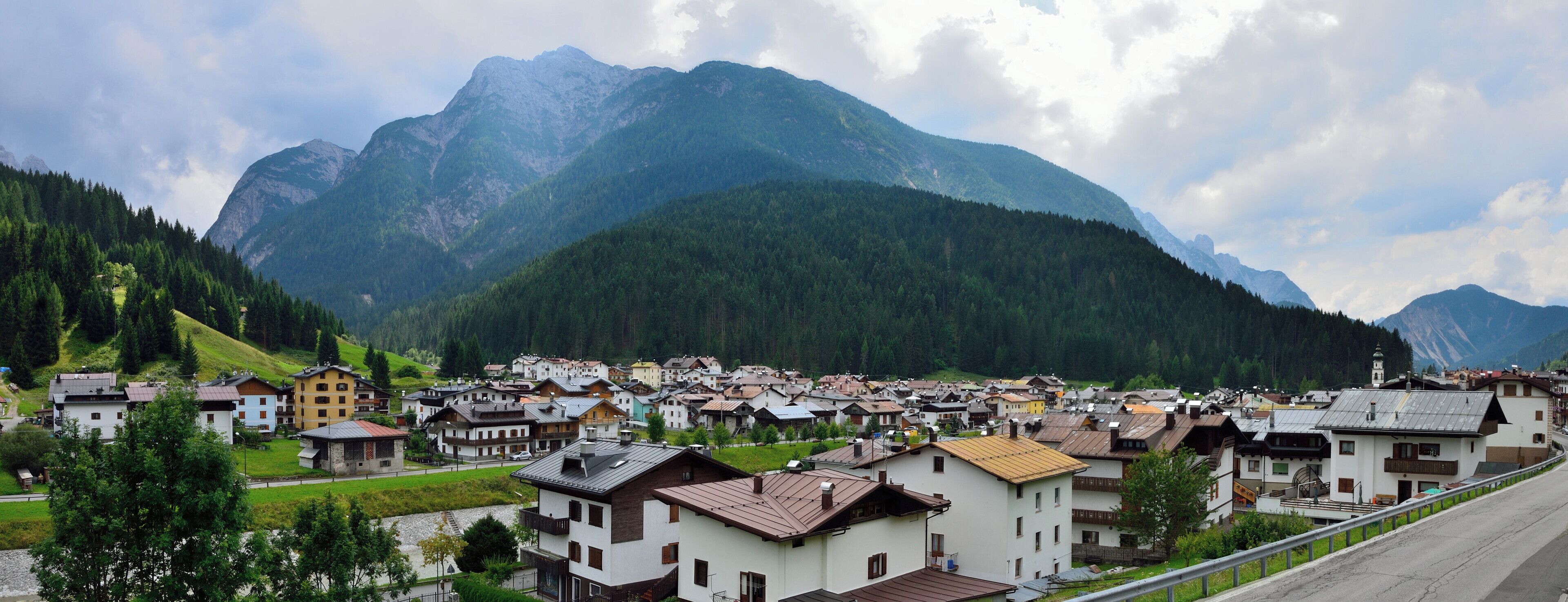 A mountain village with houses and a road in front of a mountain range.