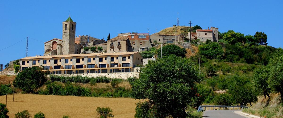 A hillside village with a prominent church tower, traditional buildings, and a road leading up the hill.