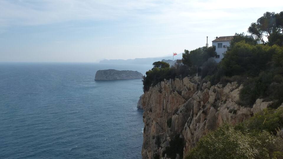 A coastal cliff with a lighthouse, rocky terrain, and a distant island.
