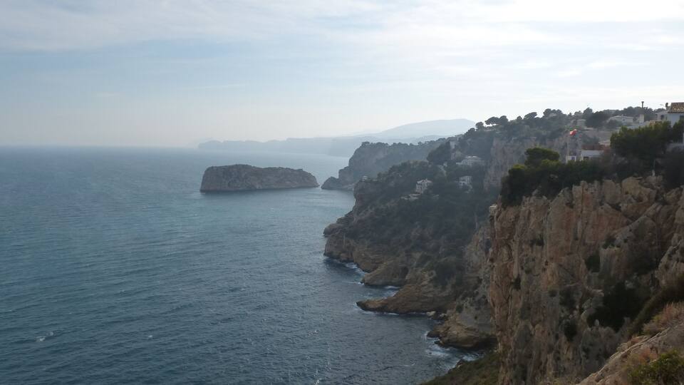 A coastal landscape with rocky cliffs, a small island, and buildings perched on the cliff edge.