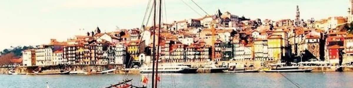 A traditional boat docked at a harbor with a cityscape in the background.