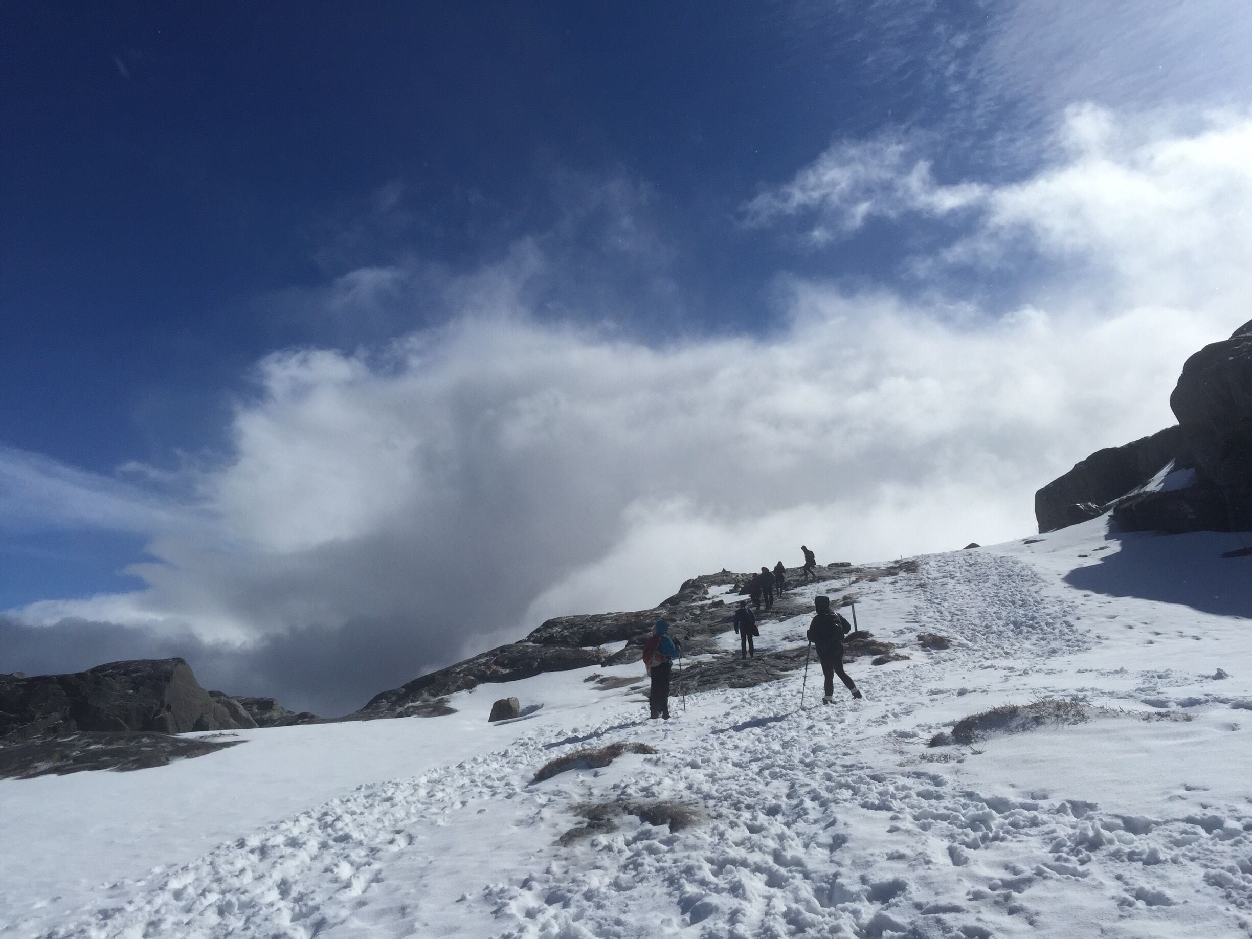 A snowy mountain with hikers and a partly cloudy sky.