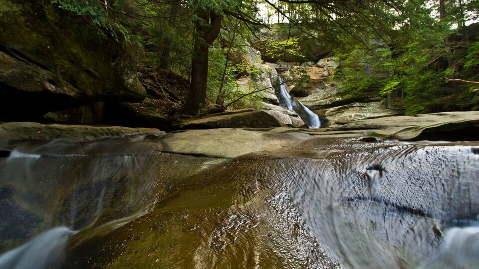 A waterfall in a forested area with large rocks and trees.
