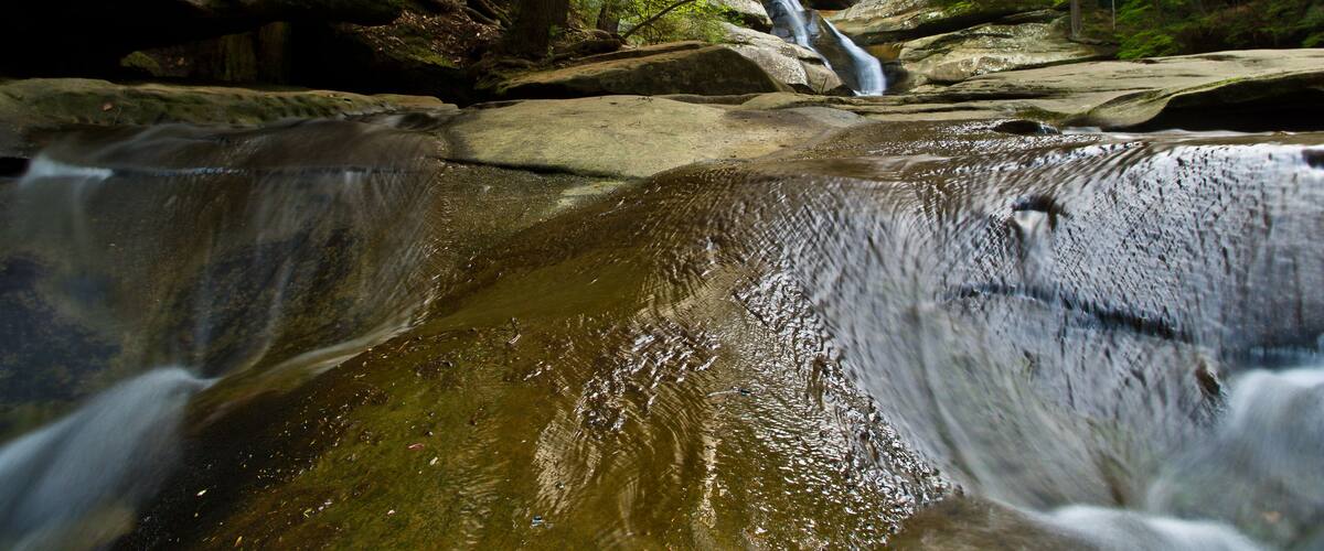 A waterfall in a forested area with large rocks and trees.
