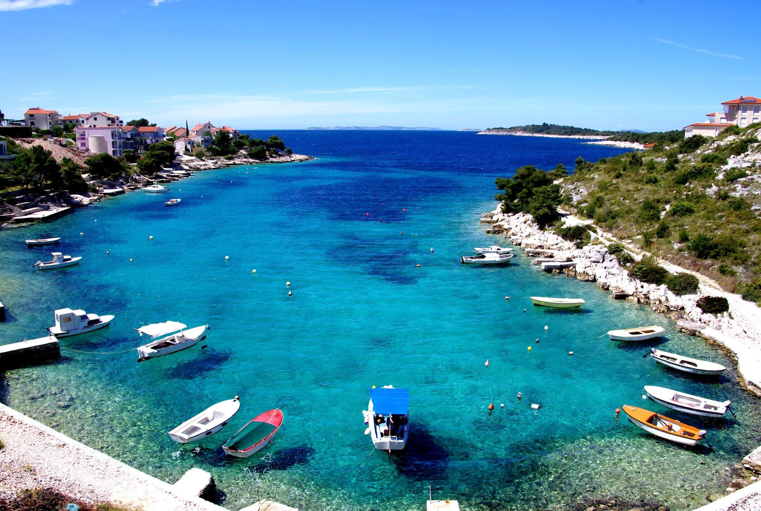 A coastal town with clear turquoise waters, boats anchored near the shore, and buildings on the hillside.