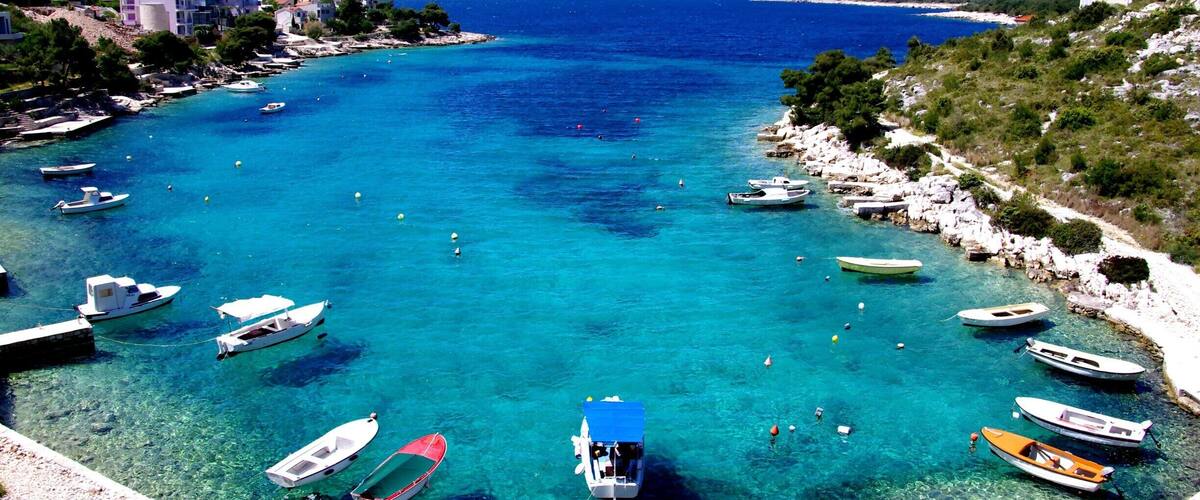 A coastal town with clear turquoise waters, boats anchored near the shore, and buildings on the hillside.
