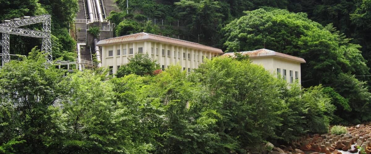 A building surrounded by lush greenery and a river with rocks.