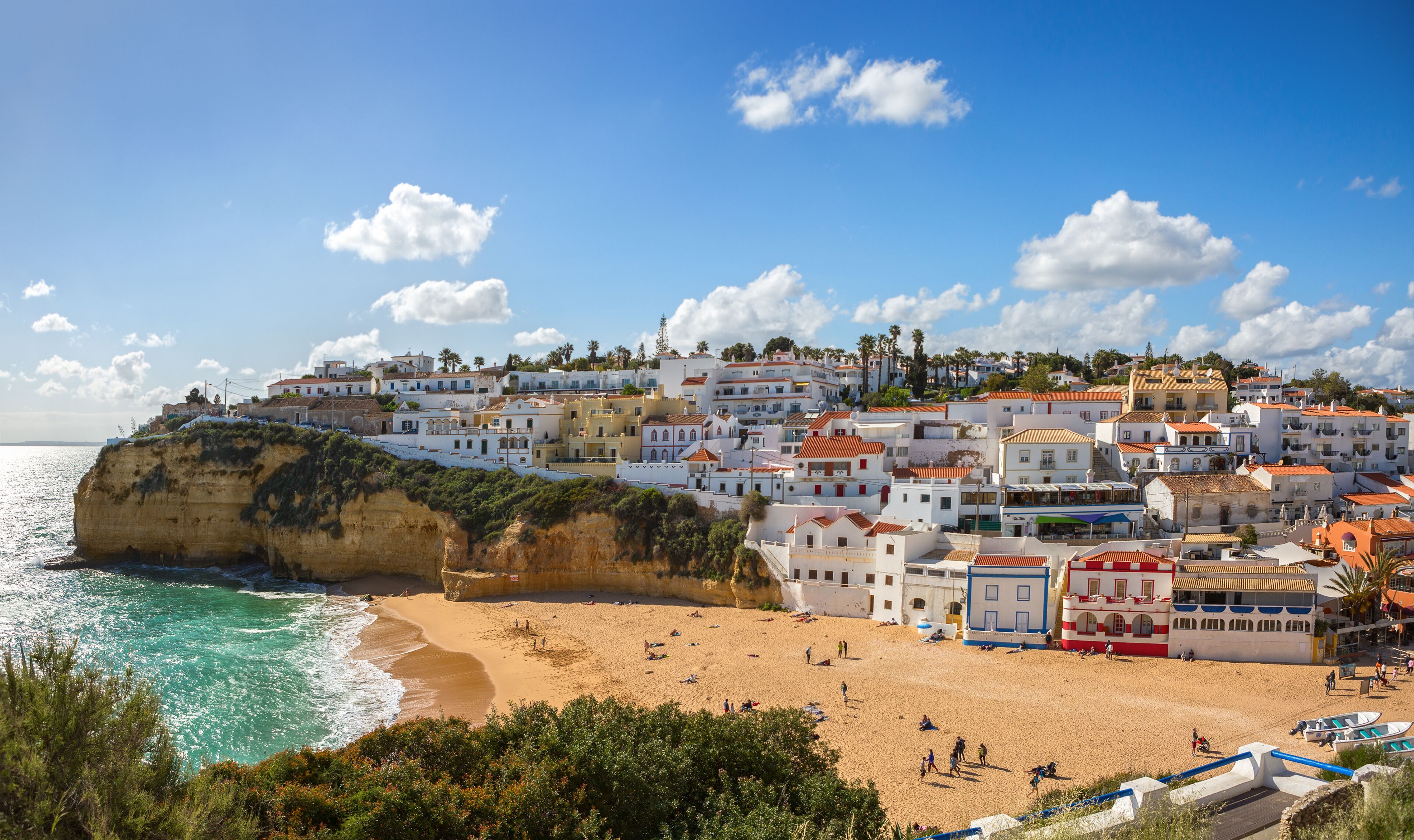 A coastal town with white buildings, a sandy beach, and a cliff overlooking the sea.