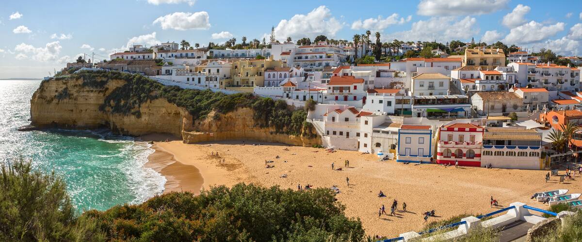 A coastal town with white buildings, a sandy beach, and a cliff overlooking the sea.