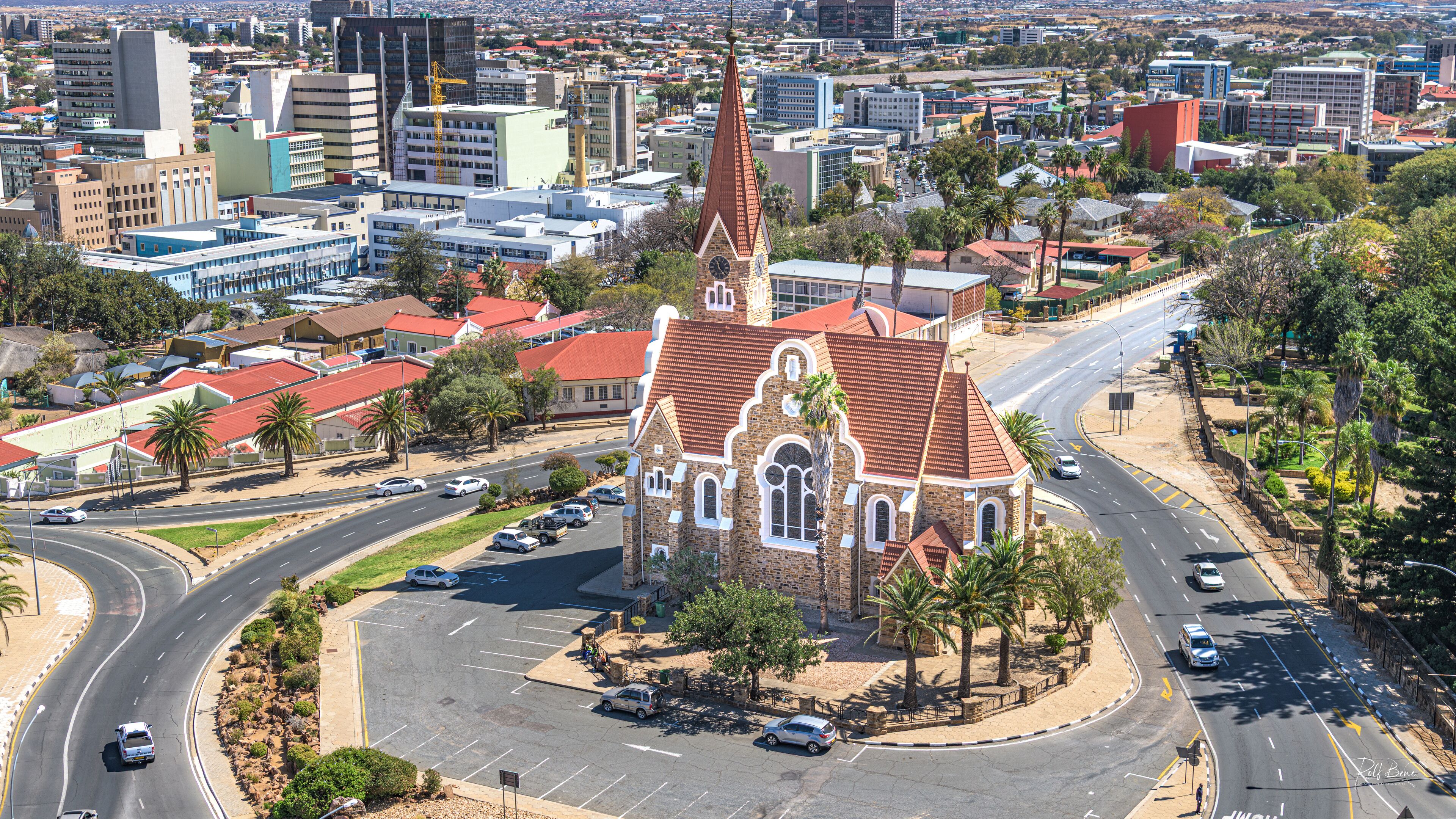 A church with a red roof and a tall steeple in a city.