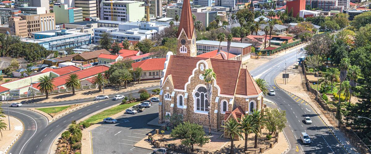 A church with a red roof and a tall steeple in a city.