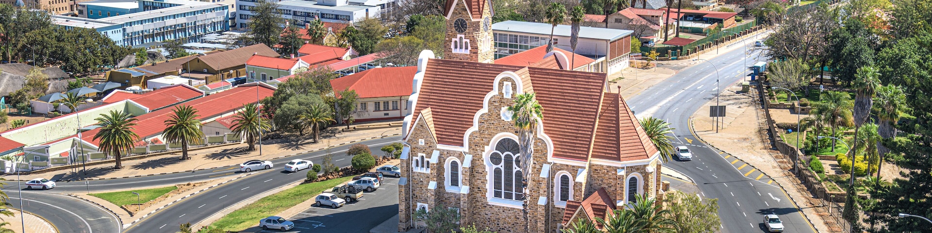 A church with a red roof and a tall steeple in a city.