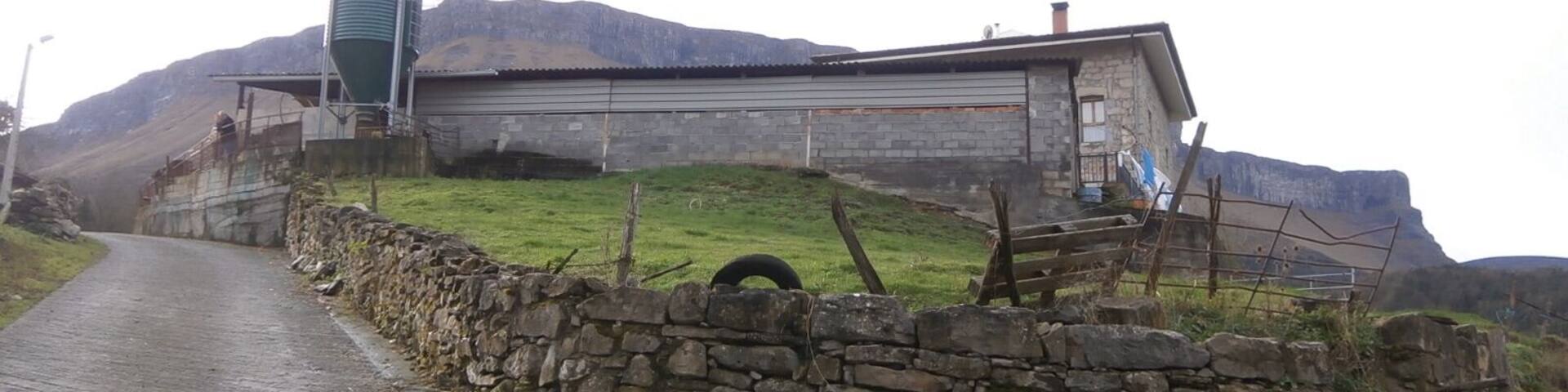 Un camino rural que lleva a un edificio de piedra con un silo verde y una pared de piedra.