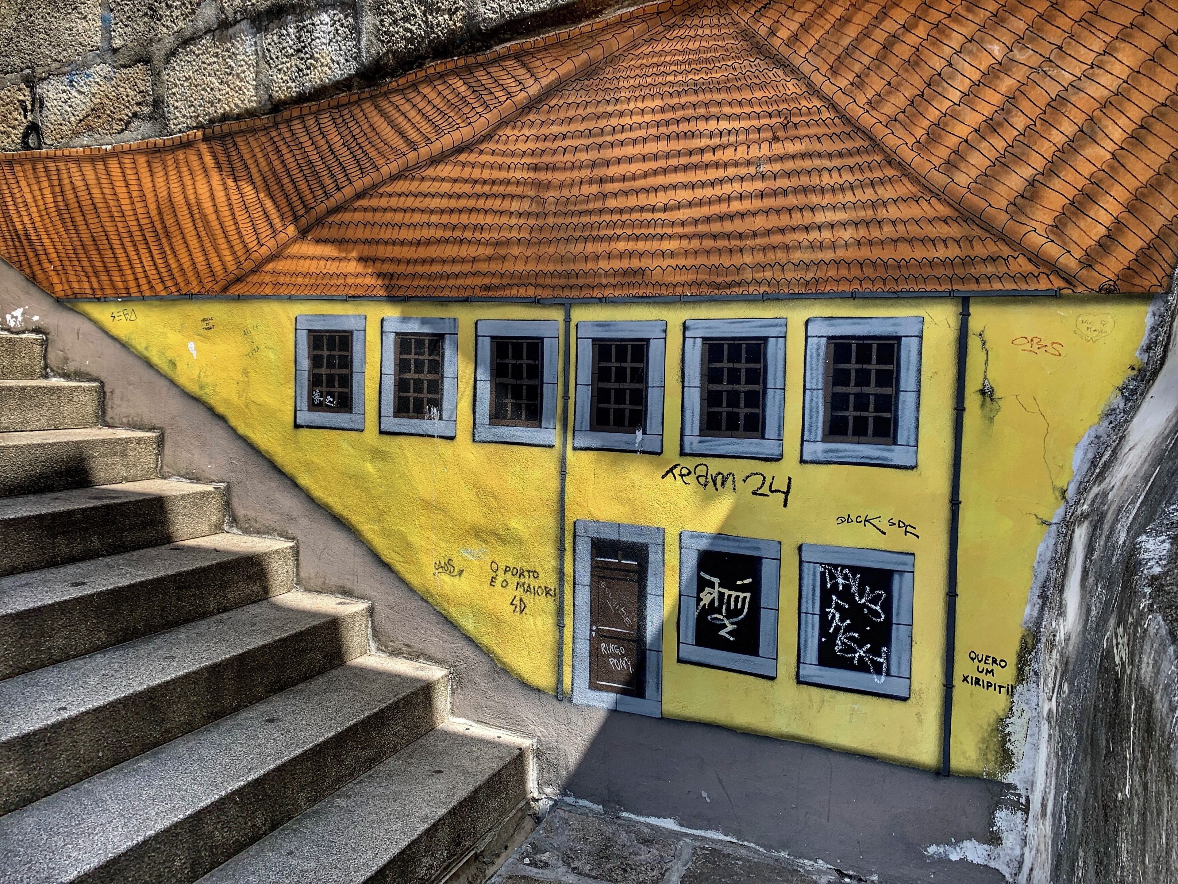 Um edifício amarelo com janelas e grafite, uma escadaria e um telhado telhado.