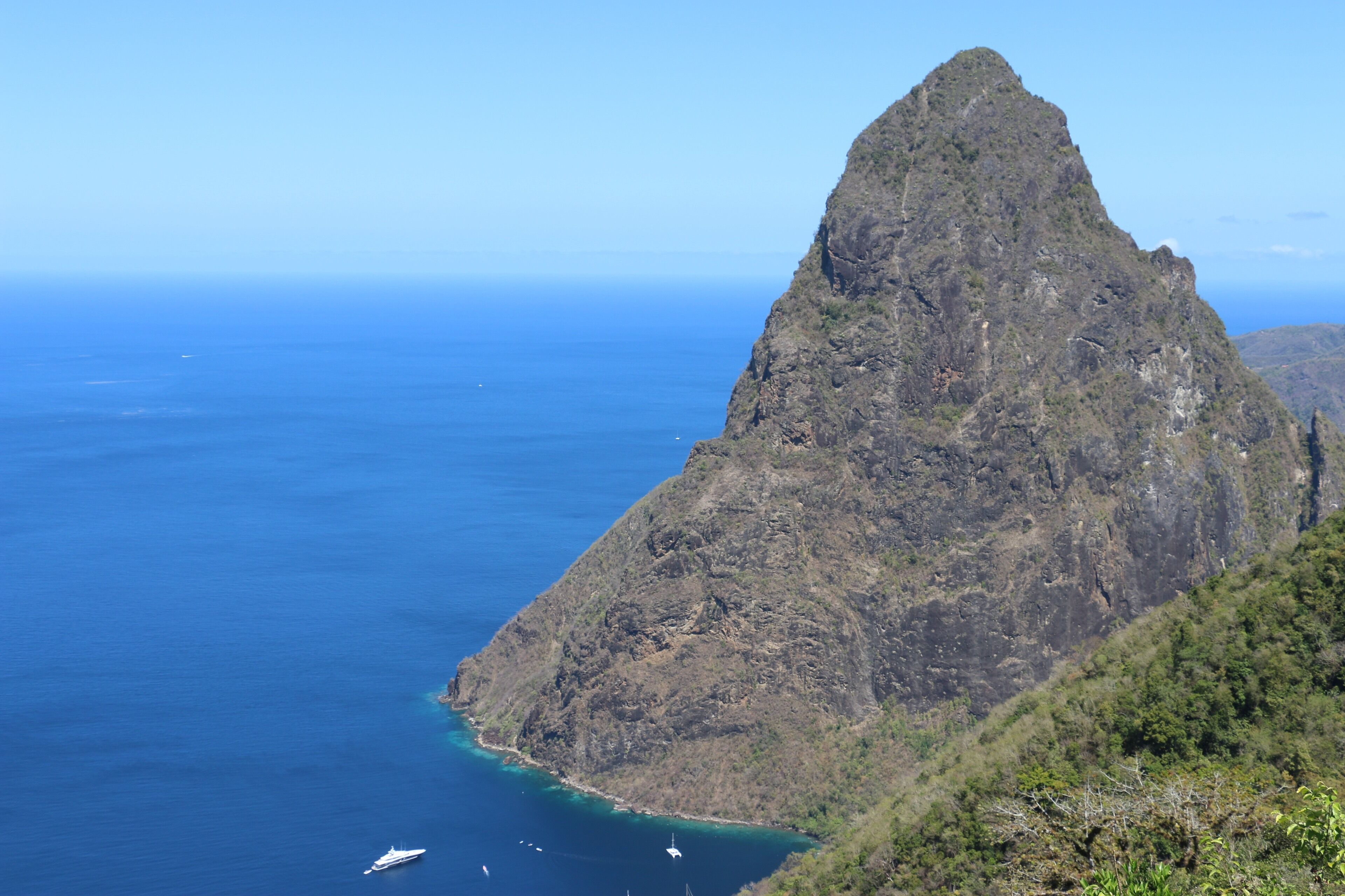 A rugged mountain peak with a clear blue sea in the foreground and a boat in the water.