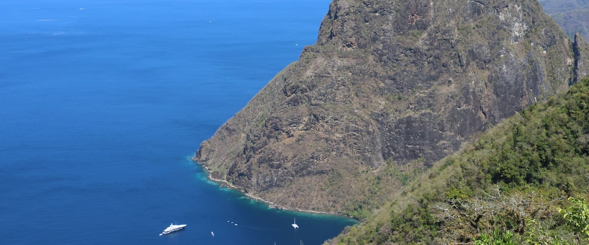 A rugged mountain peak with a clear blue sea in the foreground and a boat in the water.