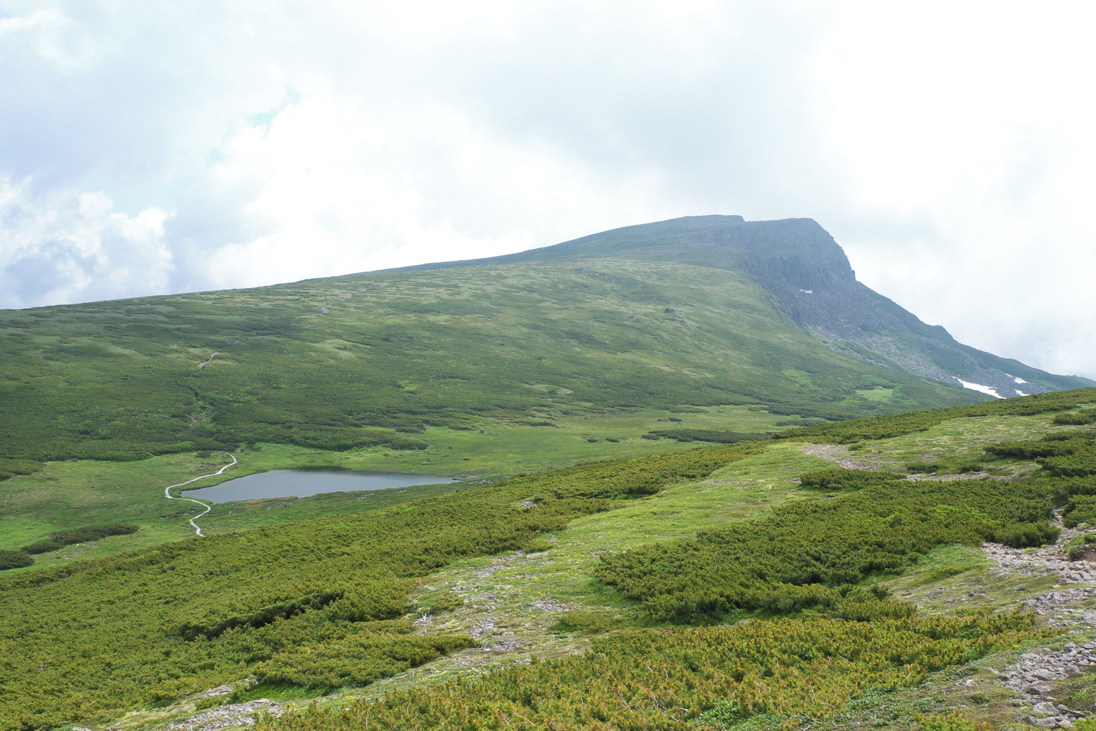 A green mountain with a lake and a winding path.