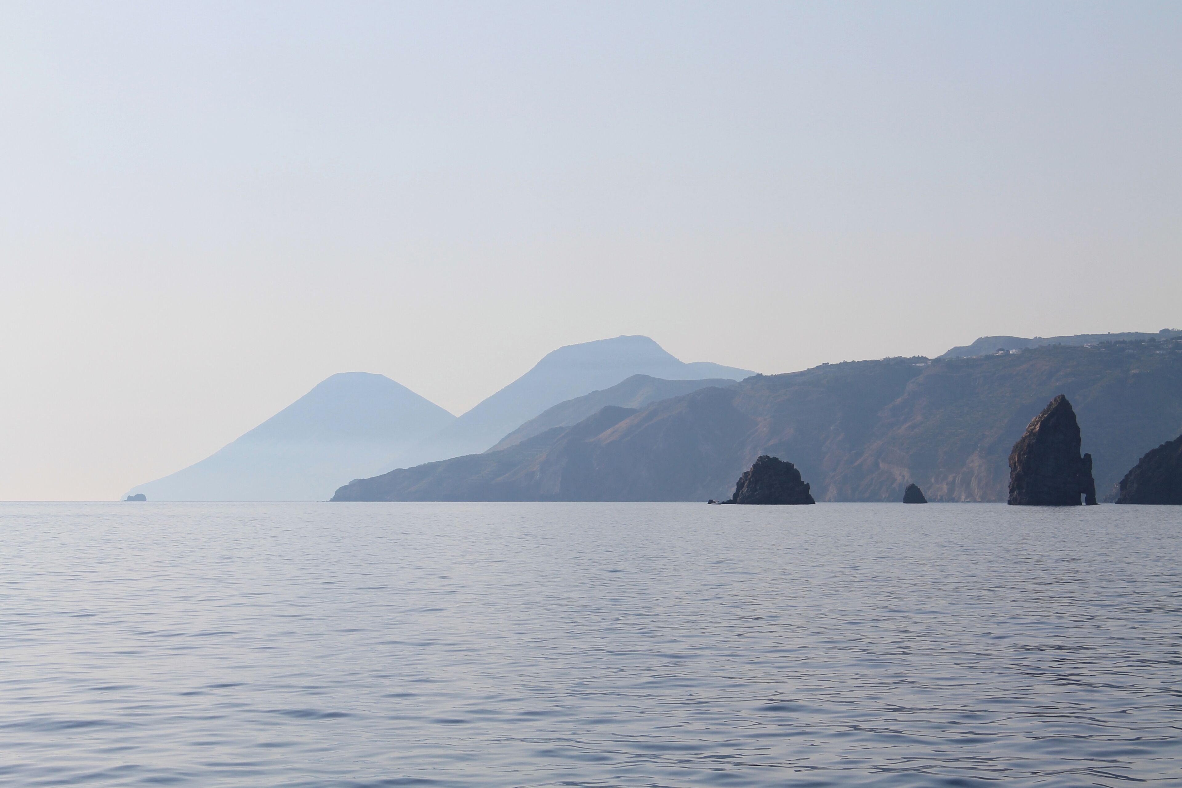 A calm sea with distant mountains and rocky outcrops.