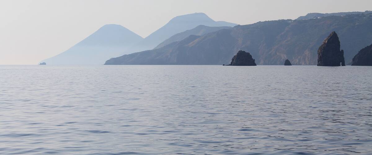 A calm sea with distant mountains and rocky outcrops.