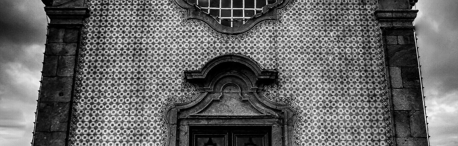Una iglesia en blanco y negro con una cruz en la parte superior, fachada de azulejos y una puerta de madera grande.