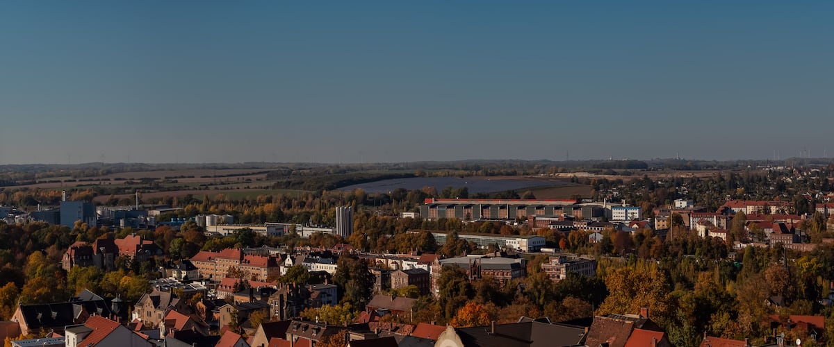 Vista panorámica de un pueblo con una mezcla de arquitectura histórica y moderna, rodeado de árboles y una masa de agua.
