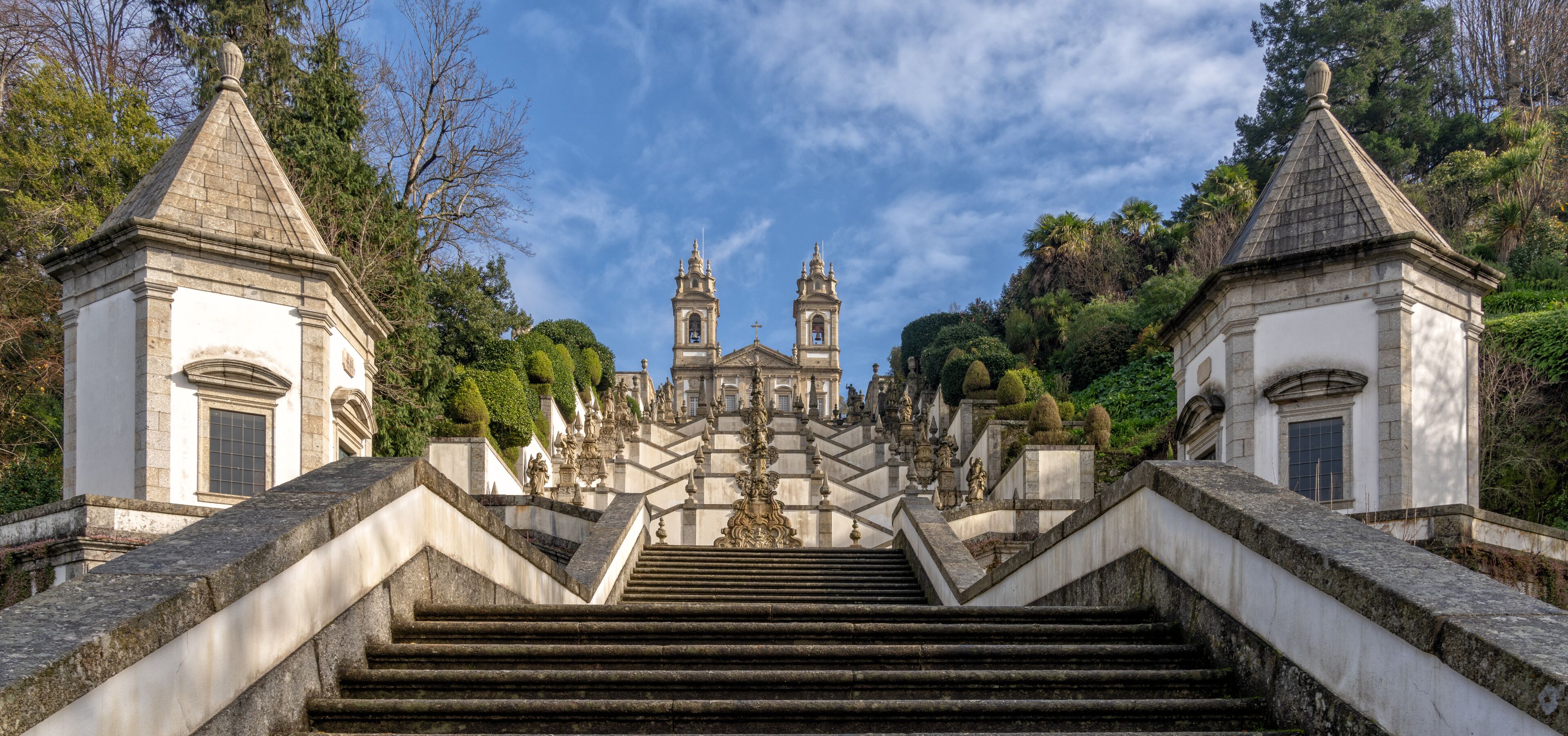 A grand staircase leading to a historic building with two towers, surrounded by lush greenery.