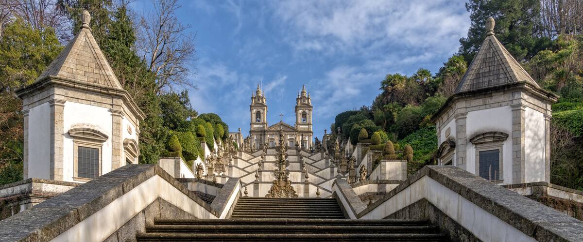 A grand staircase leading to a historic building with two towers, surrounded by lush greenery.
