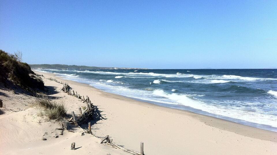 Una playa arenosa con olas rompiendo sobre la orilla y una valla de madera a lo largo del borde.