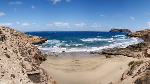 Un paysage côtier avec une plage de sable, des falaises rocheuses et une mer bleue et limpide.