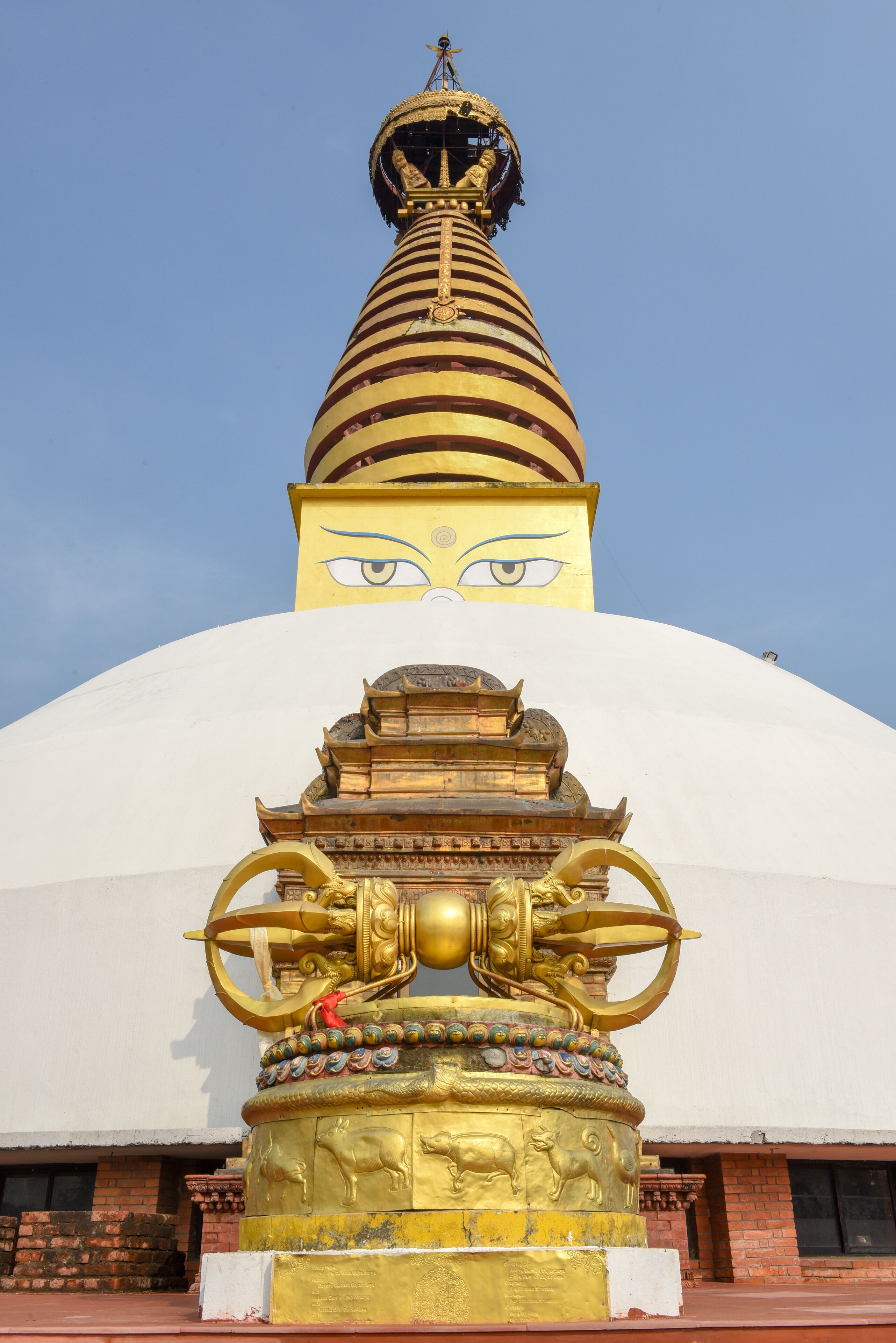 A large white stupa with a golden spire and a golden statue at its base.