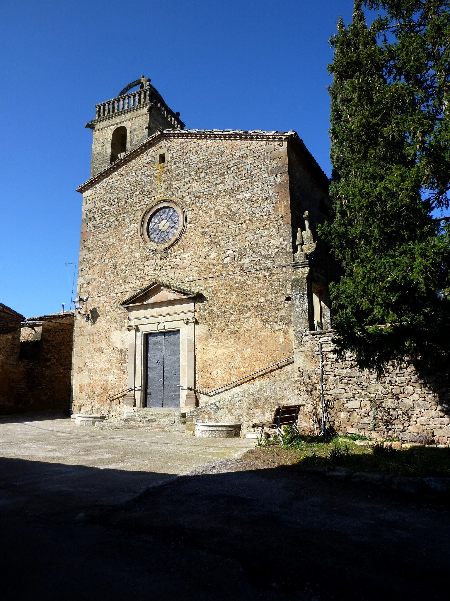 A stone church with a clock tower and a bell.
