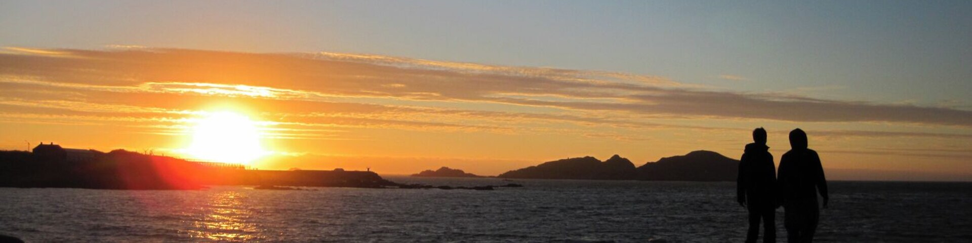 Have you experienced a 24 hour day? Hovden, on the island of Bø in Norway, is one of the places folks head to to watch the sun descend, arc against the horizon, and climb back up the other side. There are no mountains to mask the midnight sun, just open ocean. I cycled there with a couple of new friends this past summer. It was chilly, but we found ourselves taking off our shoes, increasing the sense of connection with the ground bellow us as we watched the sky above swing past. 
Have a look here for another one of my experiences soaking in the dramatic lighting of summer in the arctic: 
http://www.regenevieve.com/blog/norwegian-moments-moody-skies-dramatic-lighting/
