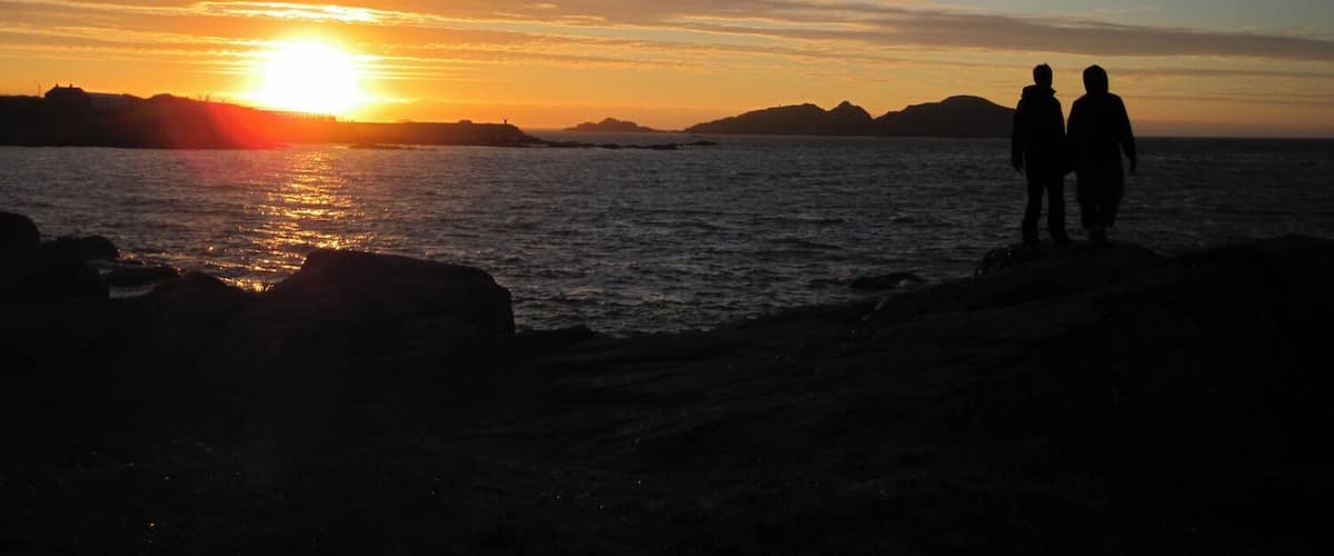 A sunset over a body of water with silhouettes of two people standing on the shore.