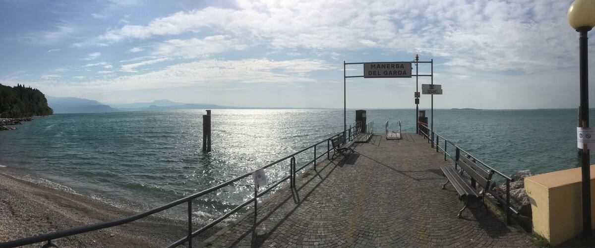 A coastal walkway with a sign reading "MANERBA DEL GARDA" and a bench.