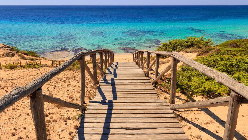 A wooden boardwalk leading to a beach with clear turquoise waters.