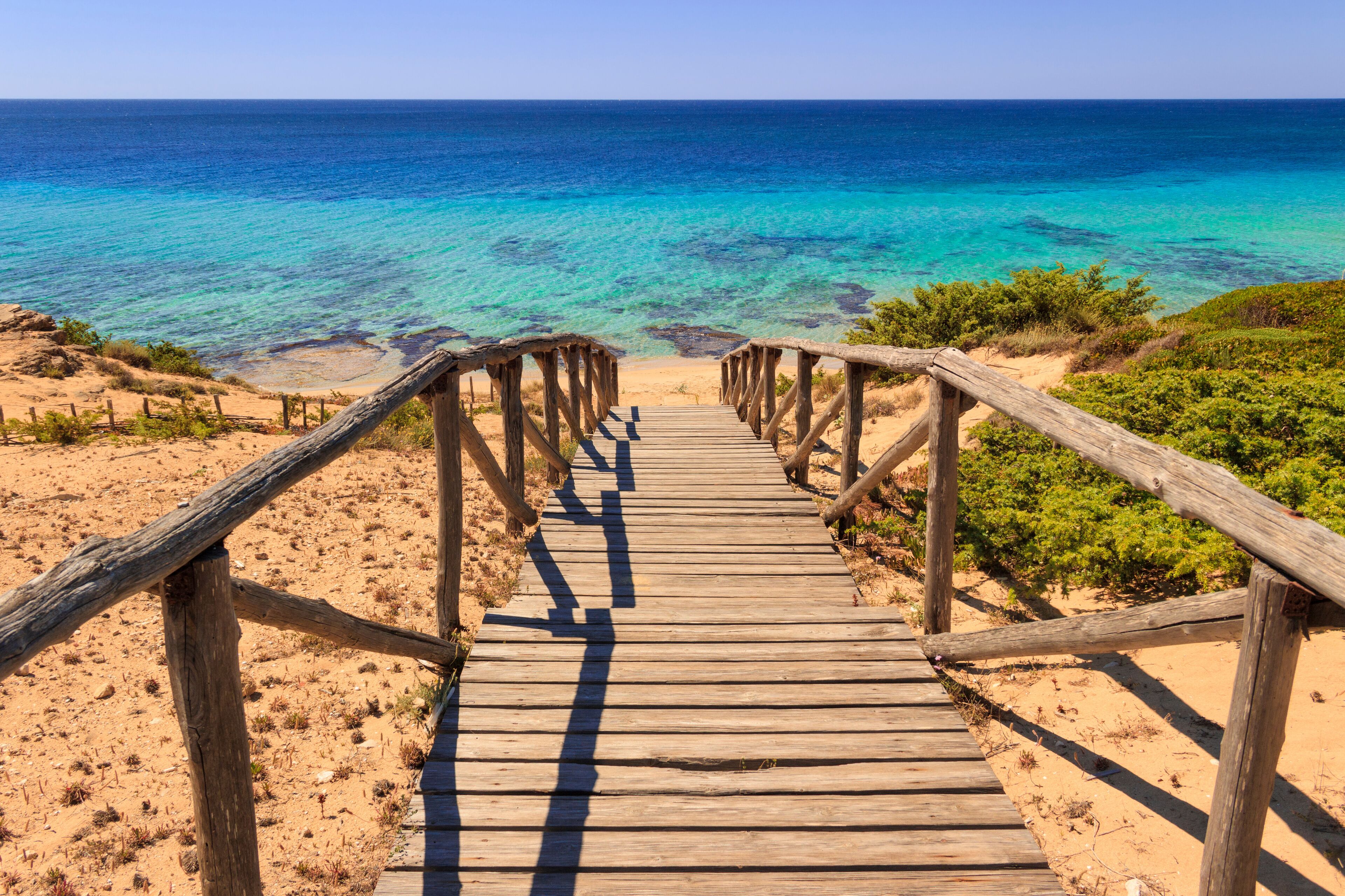 A wooden boardwalk leading to a beach with clear turquoise waters.