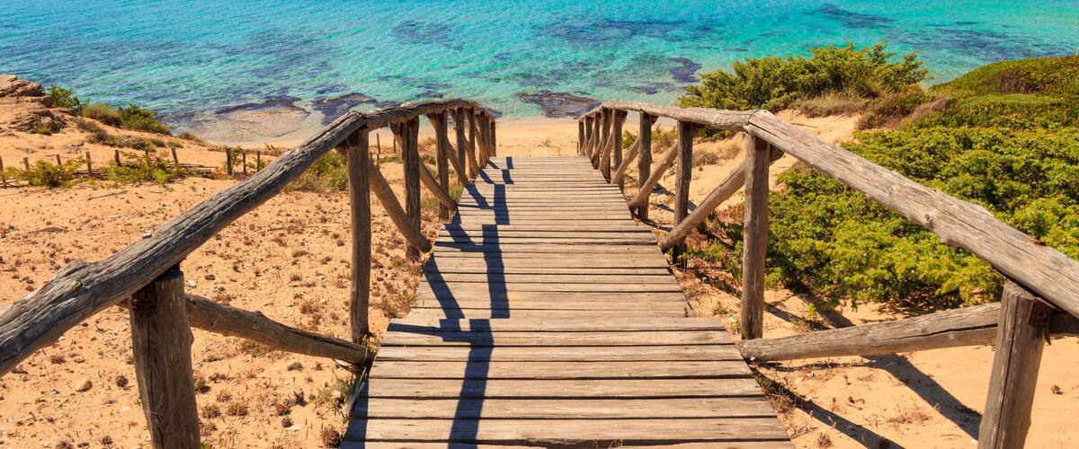 A wooden boardwalk leading to a beach with clear turquoise waters.
