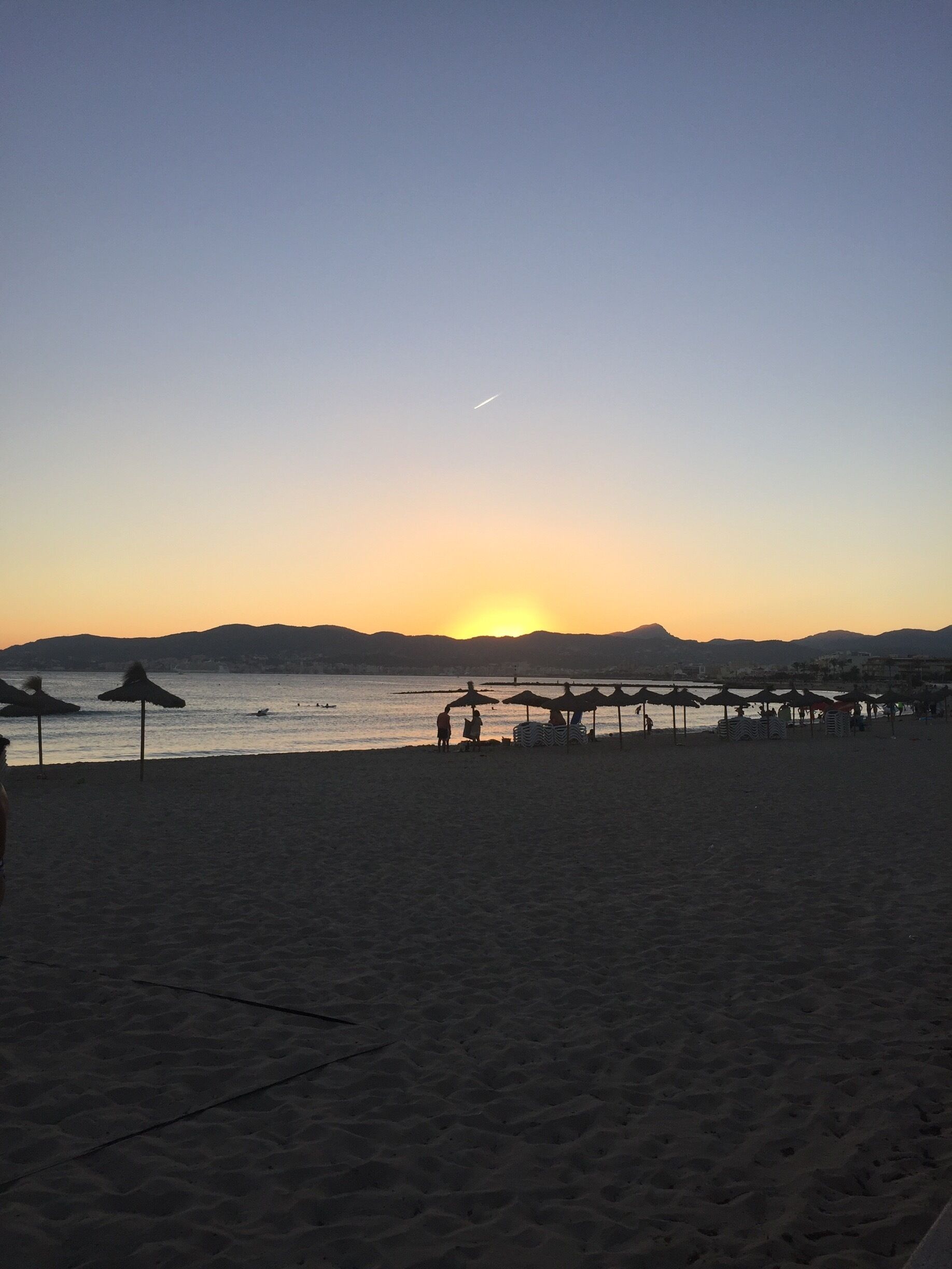 A beach at sunset with a pier extending into the water.