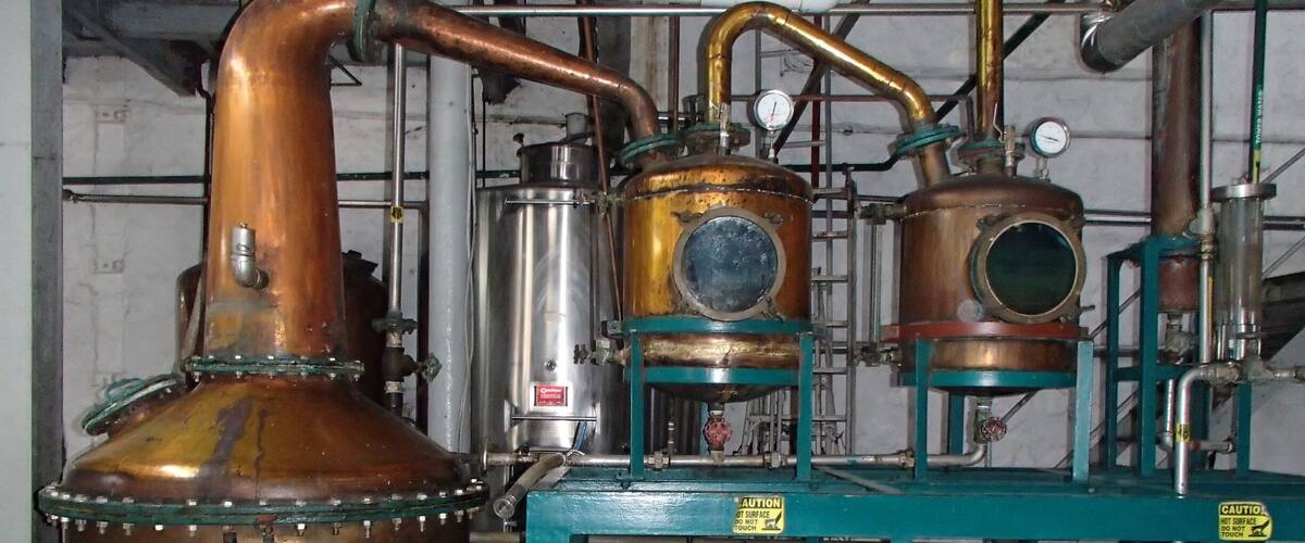 A distillation apparatus with copper components and a sign reading "John Doe".